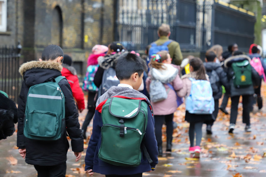 children with green backpacks on their way to school