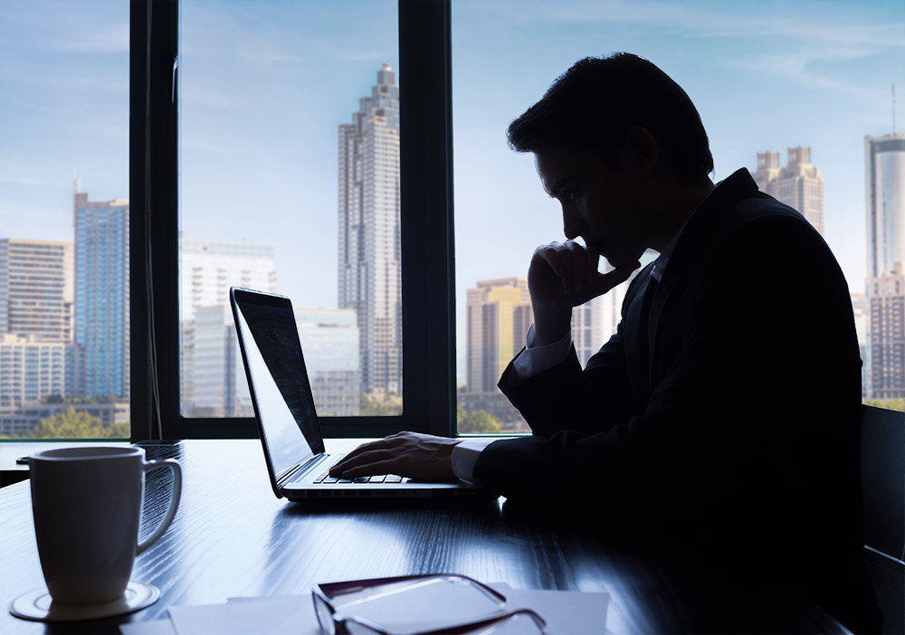 Silhouette of man looking at a laptop in an office